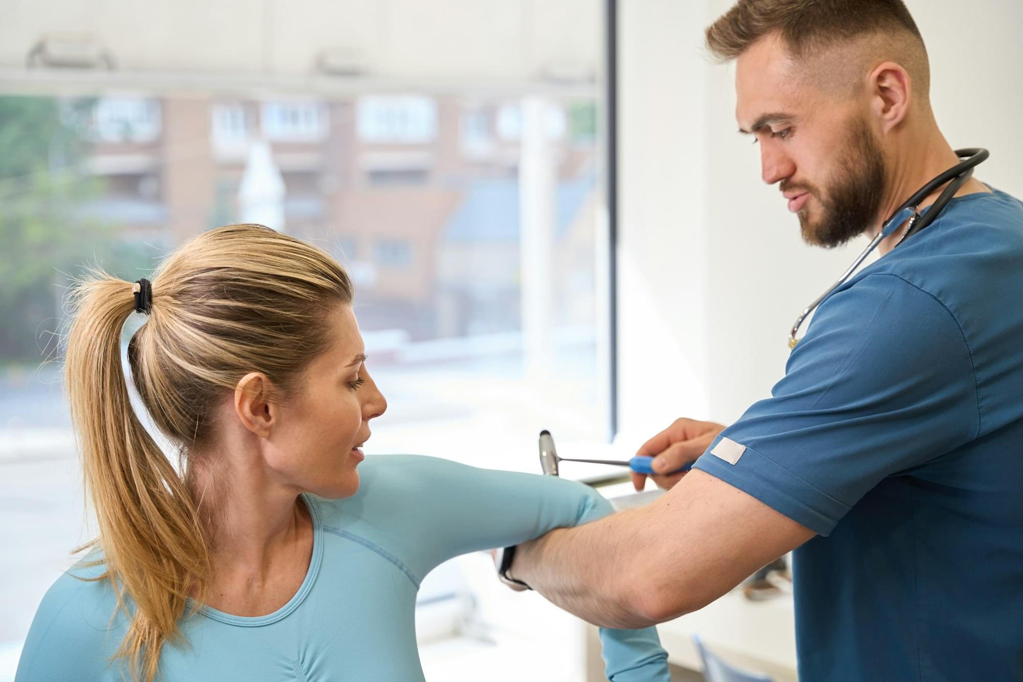 Close-up bearded neurology specialist checking female patient reflexes